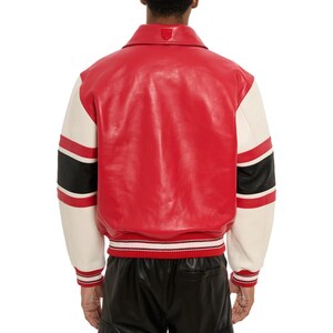 May include: Red and cream-colored varsity jacket with black stripes on the sleeves. The jacket has a red body, cream-colored sleeves, and a red and white striped ribbed hem and cuffs. A small emblem is visible on the back collar.