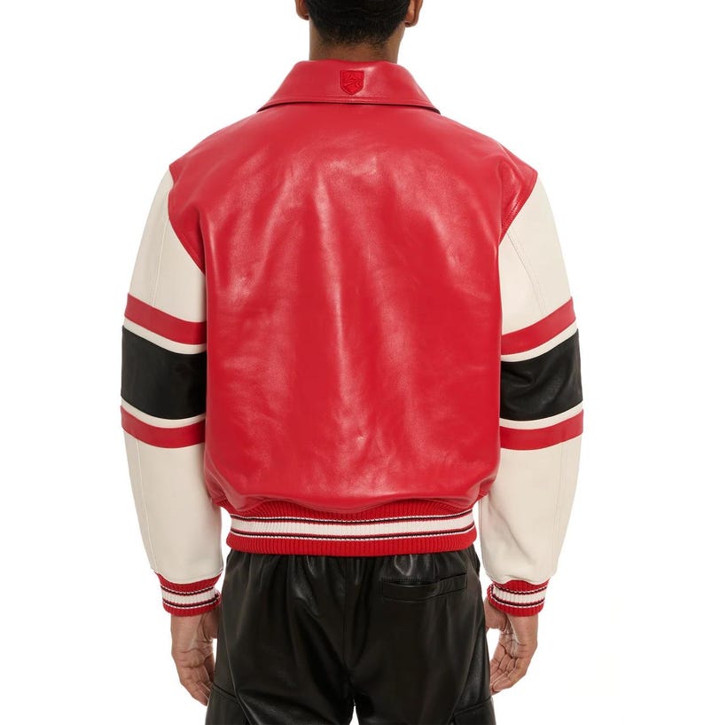 May include: Red and cream-colored varsity jacket with black stripes on the sleeves. The jacket has a red body, cream-colored sleeves, and a red and white striped ribbed hem and cuffs. A small emblem is visible on the back collar.