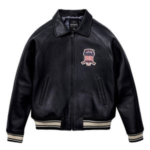 May include: Black leather bomber jacket with a zip-up front, collar, and ribbed cuffs and hem. Features a patch on the chest with the text "AVIREX" and an American flag design. The jacket has a classic, vintage style.