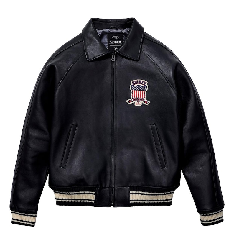 May include: Black leather bomber jacket with a zip-up front, collar, and ribbed cuffs and hem. Features a patch on the chest with the text "AVIREX" and an American flag design. The jacket has a classic, vintage style.