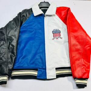 May include: A color-blocked leather jacket with black, blue, white, and red panels. The jacket features a white collar, ribbed cuffs and hem with black and white stripes, and the Avirex logo on the chest.