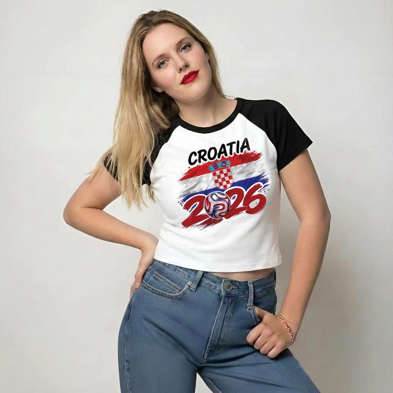 May include: A white raglan t-shirt with black sleeves featuring a graphic print that includes the text CROATIA, a red, white, and blue flag design, a red and white checkered shield emblem, and the number 2026 with a football graphic.