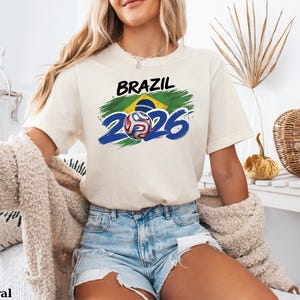 Pu&ograve; includere: Una tazza di ceramica bianca con un manico nero e la scritta "But First, Coffee" in nero, con un carattere a mano. La tazza &egrave; su una superficie bianca.