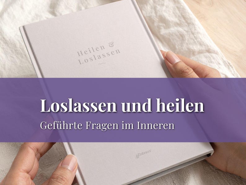May include: A light gray book with the German text "Heilen & Loslassen" and "Loslassen und heilen" in white. The book is held by two hands, resting on a white cloth. The book's title translates to "Letting go and healing".