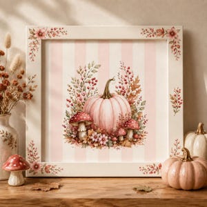 May include: A square framed wall art piece featuring a central illustration of a pale pink pumpkin surrounded by red mushrooms, autumn leaves, and berries against a light pink and white striped background, with floral accents on the frame corners.
