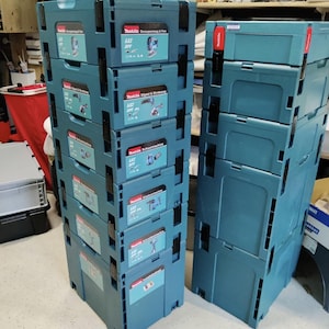 Puede incluir: Dos pilas verticales de maletines de herramientas de plástico color verde azulado de Makita Makpac. La pila de la izquierda contiene seis maletines entrelazados con etiquetas que muestran el logotipo de Makita, marcas LXT y XPT e ilustraciones.