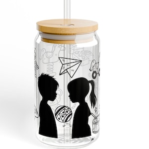 May include: A clear glass tumbler with a bamboo lid and a clear straw. The tumbler features a black and white silhouette of a boy and girl, with a patterned ball between them. The glass is decorated with playful doodles.