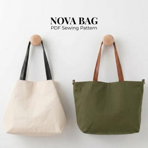 Könnte beinhalten: Zwei Tragetaschen hängen an Holzpflöcken. Eine ist cremefarben mit schwarzen Trägern, die andere olivgrün mit braunen Trägern. Der Text "NOVA BAG PDF Sewing Pattern" steht oben.