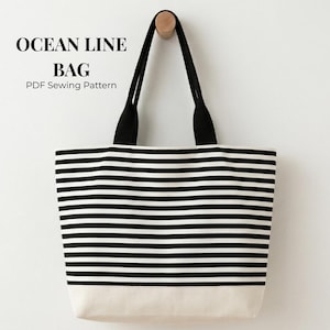 May include: A black and white striped tote bag with black handles and a beige base. The bag is suspended from a wooden peg on a white wall. The text "OCEAN LINE BAG PDF Sewing Pattern" is visible at the top.