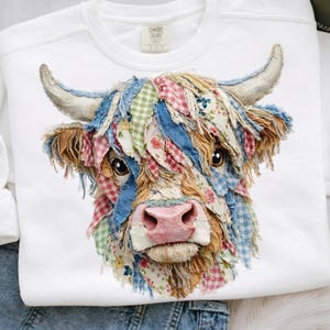 May include: A white crewneck sweatshirt featuring a central graphic of a Highland cow. The cow is composed of various fabric patches in blue denim, red and green gingham, and floral patterns, with frayed edges and a soft pink nose.