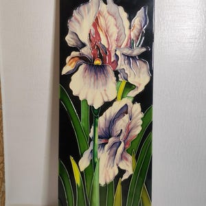 May include: A rectangular ceramic tile with a painted iris flower design. The irises have cream petals with purple and red details, set against a black background. Green leaves and stems complete the floral design.