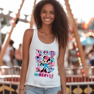 May include: White tank top featuring a colorful graphic of Minnie Mouse in various poses. The design includes the text "Disney Minnie Mouse" in a playful font, with pink, blue, and purple accents. The tank top is sleeveless.