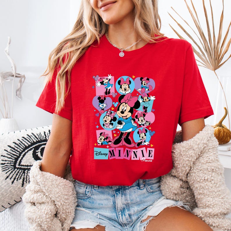 May include: A red t-shirt featuring a colorful graphic of Minnie Mouse in various poses. The design includes hearts and squares with Minnie Mouse illustrations, along with the text "Disney Minnie Mouse".