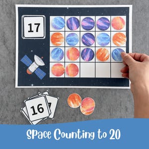 Puede incluir: Una hoja de actividades educativas sobre el espacio con un fondo azul oscuro con estrellas y una ilustración de un satélite. Incluye una cuadrícula para colocar fichas circulares y tarjetas cuadradas con los números 16 y 17.