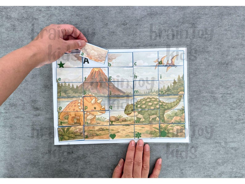 May include: A dinosaur-themed puzzle with a triceratops and ankylosaurus. The puzzle has a grid with letters and images of a volcano and flying dinosaurs. A hand is placing a puzzle piece with the letter "A".