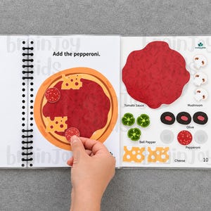 May include: A spiral-bound activity book open to a page with a pizza illustration. The text "Add the pepperoni" is above the pizza. A hand is placing a pepperoni sticker on the pizza. Other pizza toppings are displayed on the right.