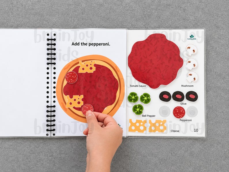 May include: A spiral-bound activity book open to a page with a pizza illustration. The text "Add the pepperoni" is above the pizza. A hand is placing a pepperoni sticker on the pizza. Other pizza toppings are displayed on the right.