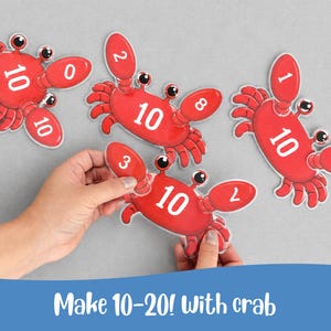 Può includere: Carte numeriche a forma di granchio rosso con il numero 10 su ciascuna e i numeri 0-9. Le carte sono tenute in mano da una persona. Il testo "Make 10-20! With crab" è in basso. Gioco di matematica educativo.