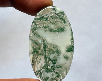 Op de afbeelding: Ovaalvormige mosagaat edelsteen met een gepolijst oppervlak. De steen heeft een mix van witte, crème en doorschijnende gebieden, met ingewikkelde groene, mosachtige insluitsels.