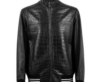 Puede incluir: Chaqueta de cuero negro con un panel frontal con textura de cocodrilo y mangas de cuero liso. Cuenta con una cremallera frontal, un cuello alzado y puños y dobladillo acanalados con rayas blancas. Una prenda de abrigo elegante.