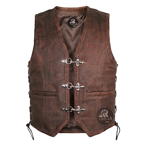 Puede incluir: Chaleco de cuero marrón con cuello en V, tres cierres plateados y dos bolsillos delanteros. El chaleco tiene un acabado envejecido y costuras decorativas en los bordes. El logotipo de la marca "AMMAR & CO" es visible.