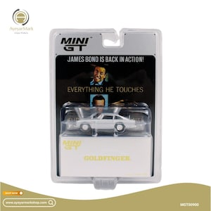 May include: A silver Mini GT model car of the Goldfinger Aston Martin DB5, packaged in a clear plastic case. The packaging features text that reads "JAMES BOND IS BACK IN ACTION!" and "EVERYTHING HE TOUCHES".