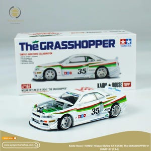 Op de afbeelding: Wit modelauto Nissan Skyline GT-R (R34) met groene en rode accenten, nummer 35 en de tekst "The GRASSHOPPER". De motorkap is open en toont de motor. Het model staat voor de doos.