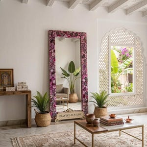 May include: A tall rectangular floor mirror featuring a frame composed of numerous polished purple and pink agate stone slices. The base of the mirror frame displays the text Crafted in Stone in a clear, dark, sans-serif font style.