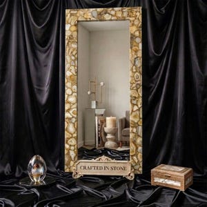 May include: A rectangular floor mirror featuring a frame composed of numerous polished, multi-toned tan and beige agate stone slices. The base of the mirror displays the text CRAFTED IN STONE in capital letters on a decorative stone plaque.