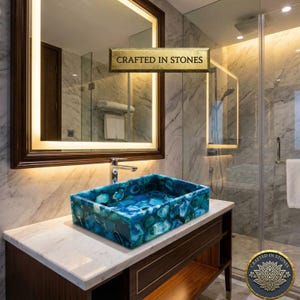 May include: A rectangular, blue and teal stone bathroom sink with a unique pattern. The sink is set on a white countertop with a dark wood cabinet. The mirror above has a warm light. The text "CRAFTED IN STONES" is visible.