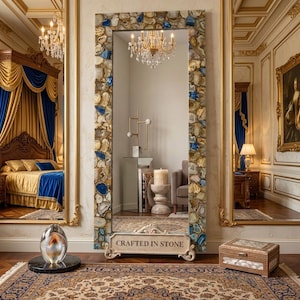 May include: A tall rectangular floor mirror featuring a frame composed of numerous polished agate slices in shades of blue, tan, and white. The base of the mirror is made of light-colored stone with the text "CRAFTED IN STONE" engraved on the front.