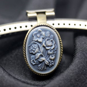 May include: A silver and gold oval-shaped clasp with a blue and white floral design. The clasp is attached to a silver metal strap.