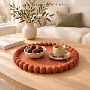May include: A round, terracotta-colored tray with a textured, beaded border. On the tray sits a speckled ceramic bowl filled with dark chocolate truffles and a matching ceramic cup and saucer containing coffee with a small gold spoon.