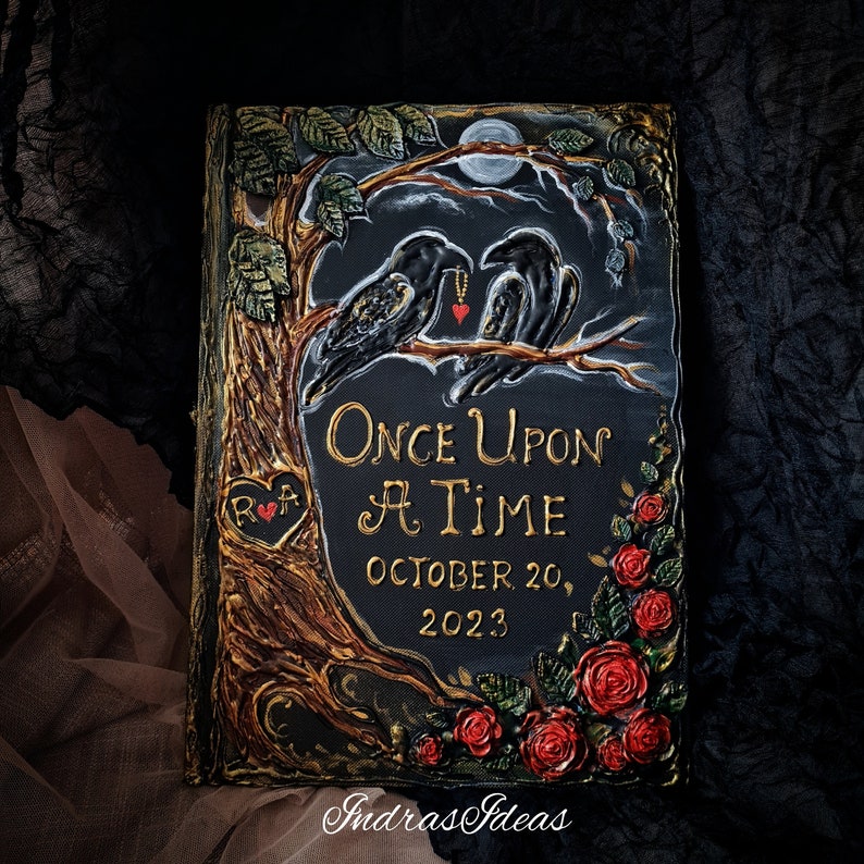 May include: A black book with a gold embossed design of a tree with two ravens perched on branches. The book has the words "Once Upon A Time" and the date "October 20, 2023" written in gold lettering. The book is decorated with red roses and leaves.