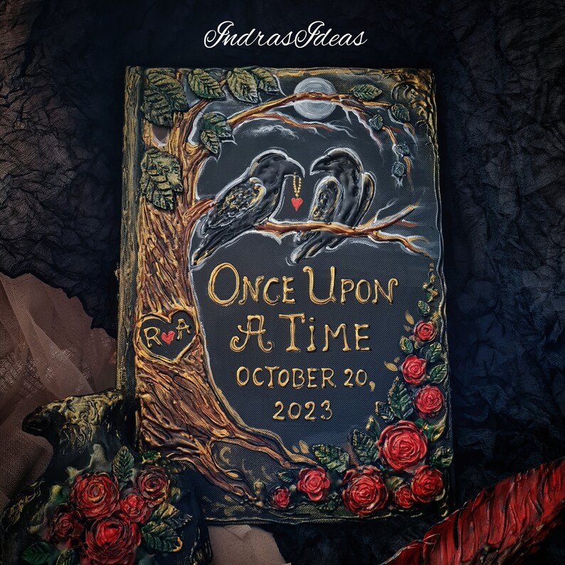 May include: A black book with a gold inscription that reads "Once Upon A Time" and "October 20, 2023". The book is decorated with a tree, two black birds, and red roses.
