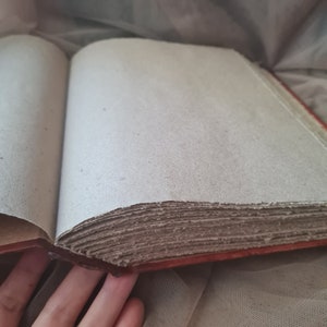 May include: A brown leather-bound journal with blank pages. The journal is open to reveal the pages, which are made of a thick, textured paper.