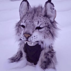 May include: A detailed snow leopard mask. The mask has a realistic design with grey and white fur, black markings, and visible teeth. The background is a snowy environment.