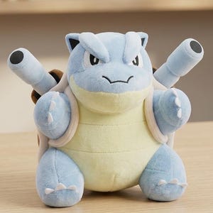 May include: A plush Blastoise toy, a water-type Pokémon, is displayed. The toy features a light blue body, a yellow belly, and two cannons on its back. It is set on a wooden surface.