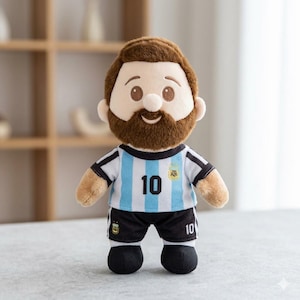 May include: A plush doll featuring a brown-haired figure with a beard, wearing a light blue and white striped soccer jersey with the number 10 and a small emblem, paired with black shorts featuring the number 10 and a small emblem on the leg.
