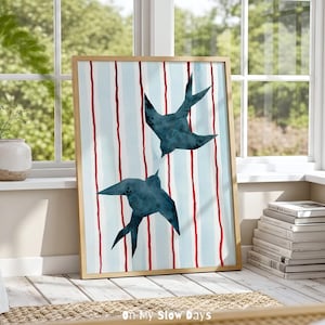 May include: A framed art print featuring two stylized blue swallows against a backdrop of vertical light blue stripes with red accents. The artwork is in a natural wood frame and is displayed near a window. The text "On My Slow Days" and "HAND-PAINTED PRINTABLE ART" is visible.