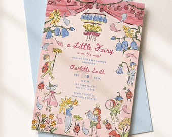May include: A rectangular baby shower invitation card on a light blue envelope. The card features a pink background with watercolour illustrations of fairies, ladybugs, and flowers. Text reads: a Little Fairy is on the way! Charlotte Smith, Dec 18 2026.