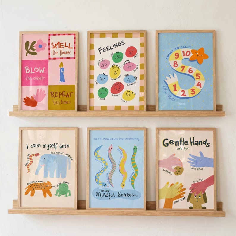May include: Six framed art prints with colourful illustrations and text, displayed on a wooden shelf. The prints feature themes of feelings, calming techniques, and mindfulness. The prints have playful designs and educational content, displayed against a white wall.