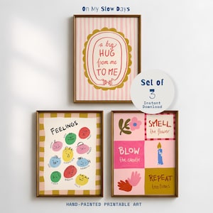 May include: A set of three wall art prints titled On My Slow Days. One print features a pink striped background with a gold scalloped frame and the text a big HUG from me TO ME. Another shows colourful emotion icons labelled Feelings. The third shows instructions to smell the flower, blow the candle, and repeat ten times.