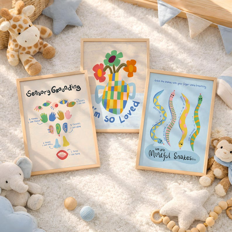 May include: Three framed art prints with light wood frames. One print says "Sensory Grounding" with colourful illustrations. Another says "I'm so Loved" with a vase of flowers. The third says "We are Mindful Snakes" with snake illustrations.