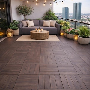 Może przedstawiać: Scena na patio na zewnątrz z ciemnobrązową drewnianą podłogą. Szara sofa z beżowymi poduszkami stoi obok okrągłego wiklinowego stolika kawowego ze świecami. Doniczkowe rośliny i łańcuchy świetlne dodają klimatu, z panoramą miasta w tle.