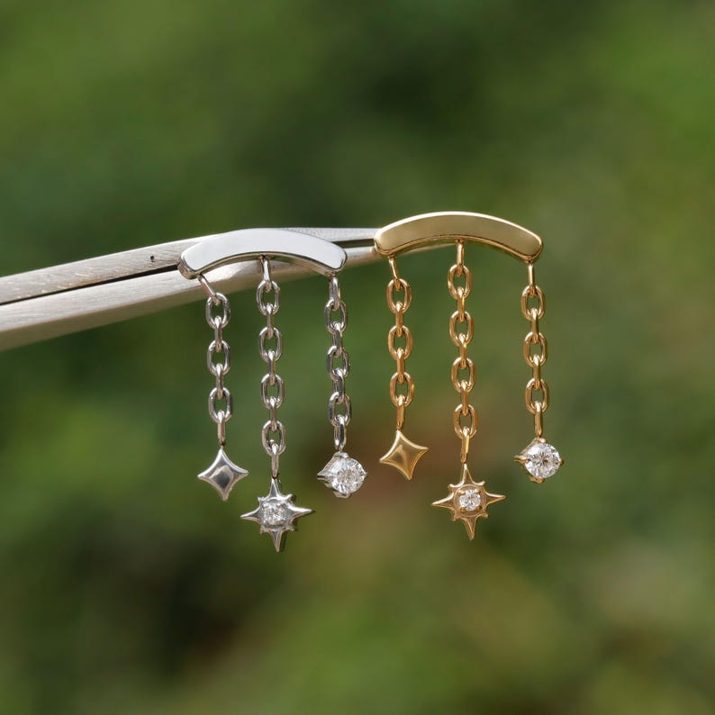 Peut inclure: Gros plan de deux paires de boucles d'oreilles. Une paire est argent&eacute;e, l'autre dor&eacute;e. Chaque boucle d'oreille a une barre incurv&eacute;e avec des cha&icirc;nes pendantes. Les cha&icirc;nes se terminent par des breloques en forme d'&eacute;toile et de diamant.
