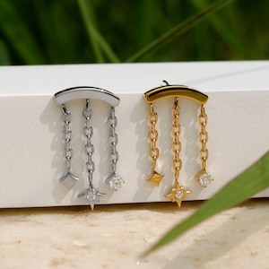 Peut inclure: Deux boucles d'oreilles, une argent&eacute;e et une dor&eacute;e, chacune avec un dessus incurv&eacute; et trois cha&icirc;nes pendantes. La boucle d'oreille argent&eacute;e a un charm en forme de losange, un charm en forme d'&eacute;toile et une gemme transparente. La boucle d'oreille dor&eacute;e a un charm en forme d'&eacute;toile, un charm en forme de losange et une gemme transparente.