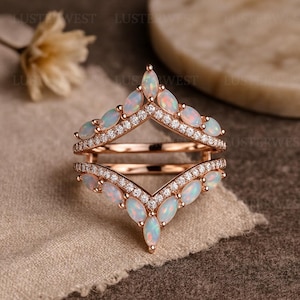 Può includere: Un anello in oro rosa con un design a doppia fascia. L'anello presenta accenti di opale e diamanti. Le pietre di opale sono a taglio marquise e disposte a forma di V. I diamanti sono piccoli e incastonati a pavé lungo la fascia.