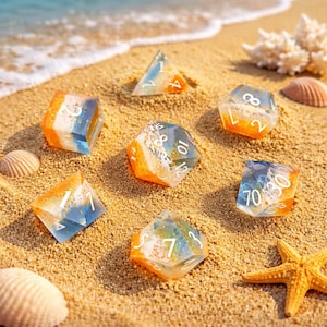 Puede incluir: Un conjunto de dados de resina coloridos con detalles en naranja, azul y blanco, esparcidos en una playa de arena. Los dados tienen varias formas, incluyendo un d4, d6, d10, d12 y d20. También se ven conchas marinas y una estrella de mar.