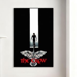 Op de afbeelding: Een ingelijste poster met een zwarte achtergrond en een witte verticale streep. Een figuur in het zwart loopt naar de kijker toe. Daaronder een gestileerde kraafgrafiek en de titel "The Crow" in het rood.